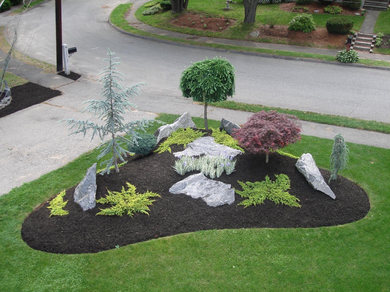 Aerial view of curved garden island with black mulch, ornamental trees, and boulders